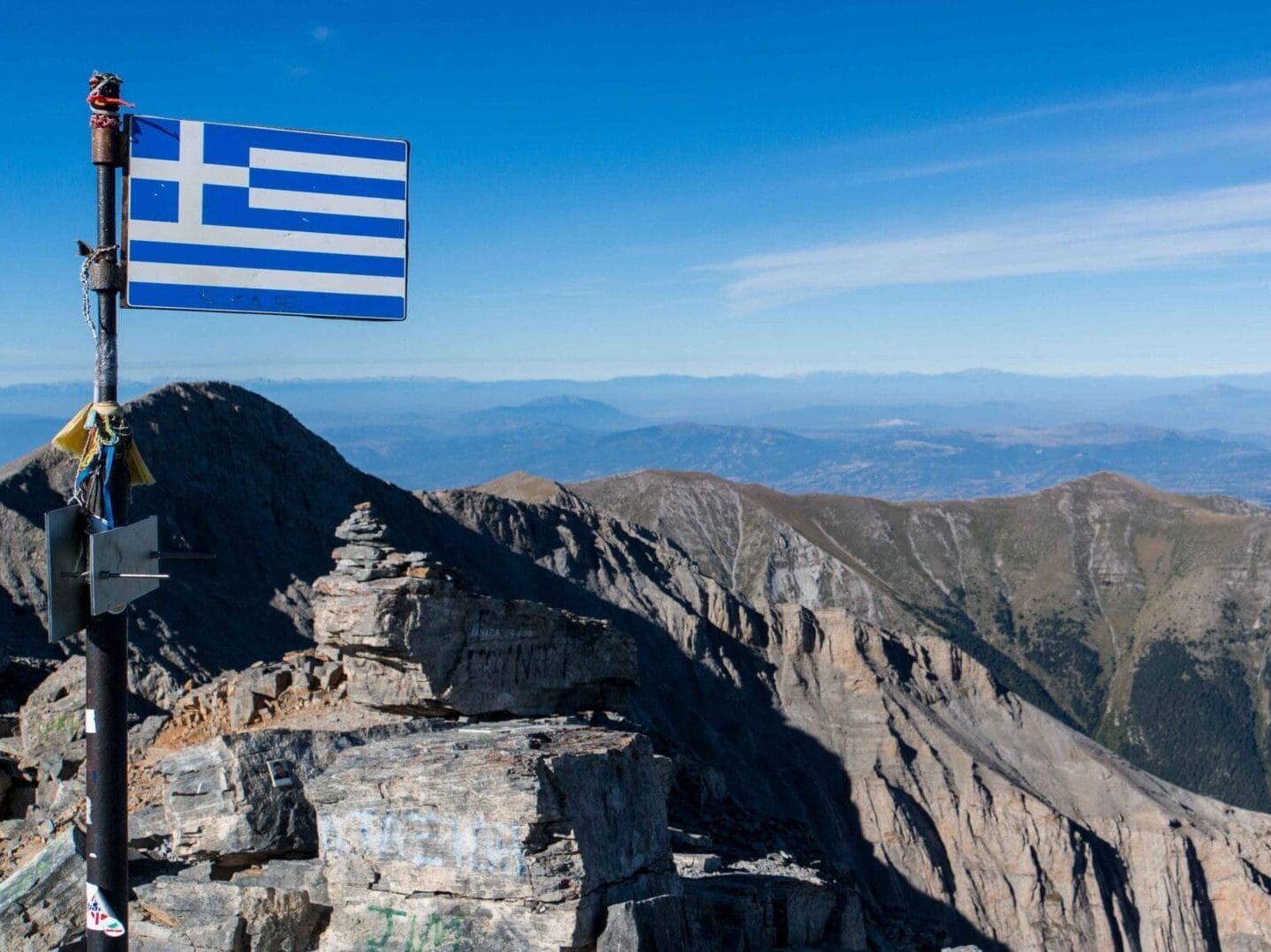 Auf dem Mytikas Gipfel mit griechischer Flagge im Vordergrund und dem Olymp Gebirge im Hintergrund